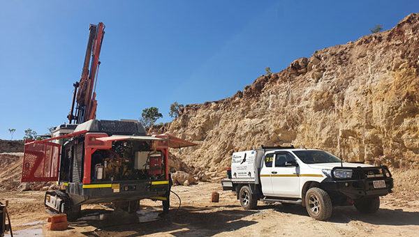 A tracked drill rig with its engine canopy open, parked beside a Falcon Diesel service ute at the foot of a cut rock face
