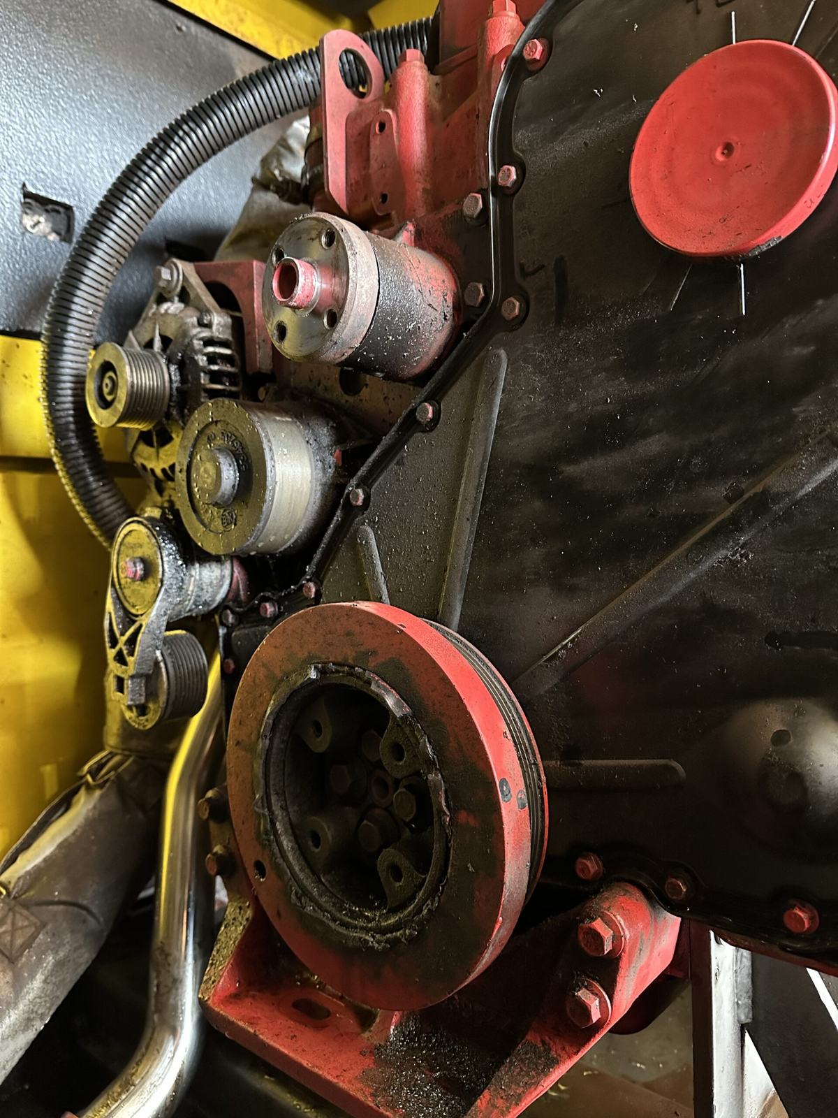 Close-up of the front of a diesel engine, with the crankshaft damper, belt idler pulleys and alternator exposed