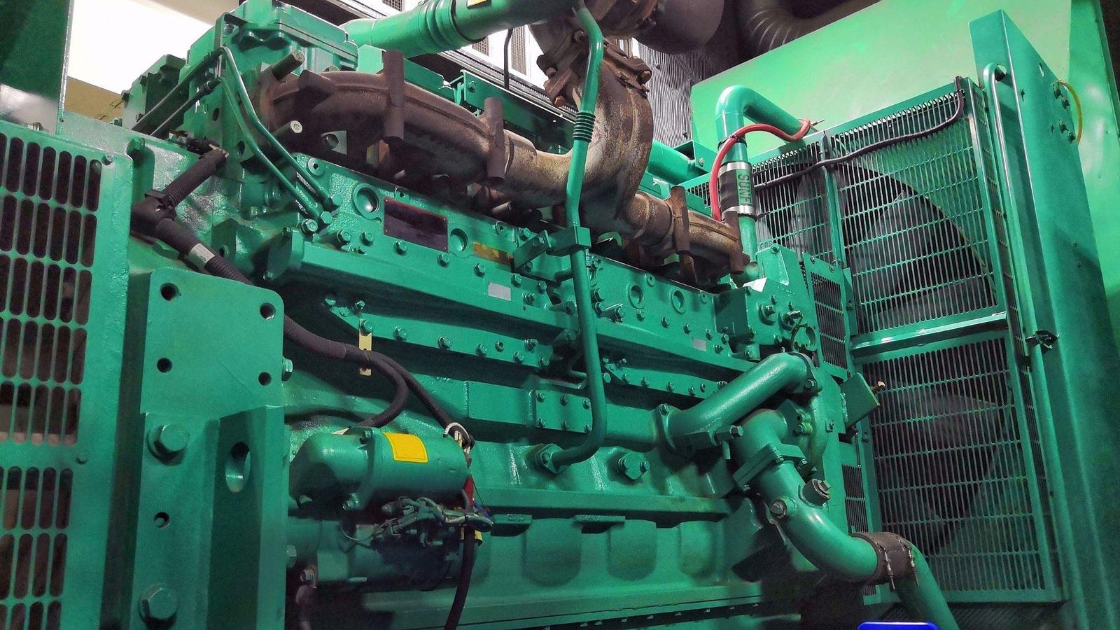 Close-up of a green in-line diesel engine on a generator set, exhaust manifold along the top and the radiator fan guard at one end