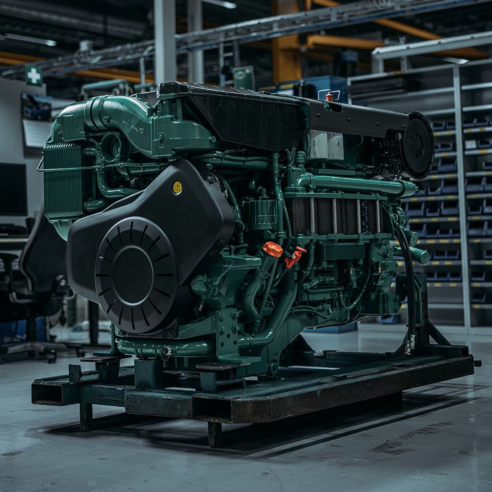 A green Volvo Penta marine diesel engine bolted to a steel transport skid on a warehouse floor, with parts shelving behind