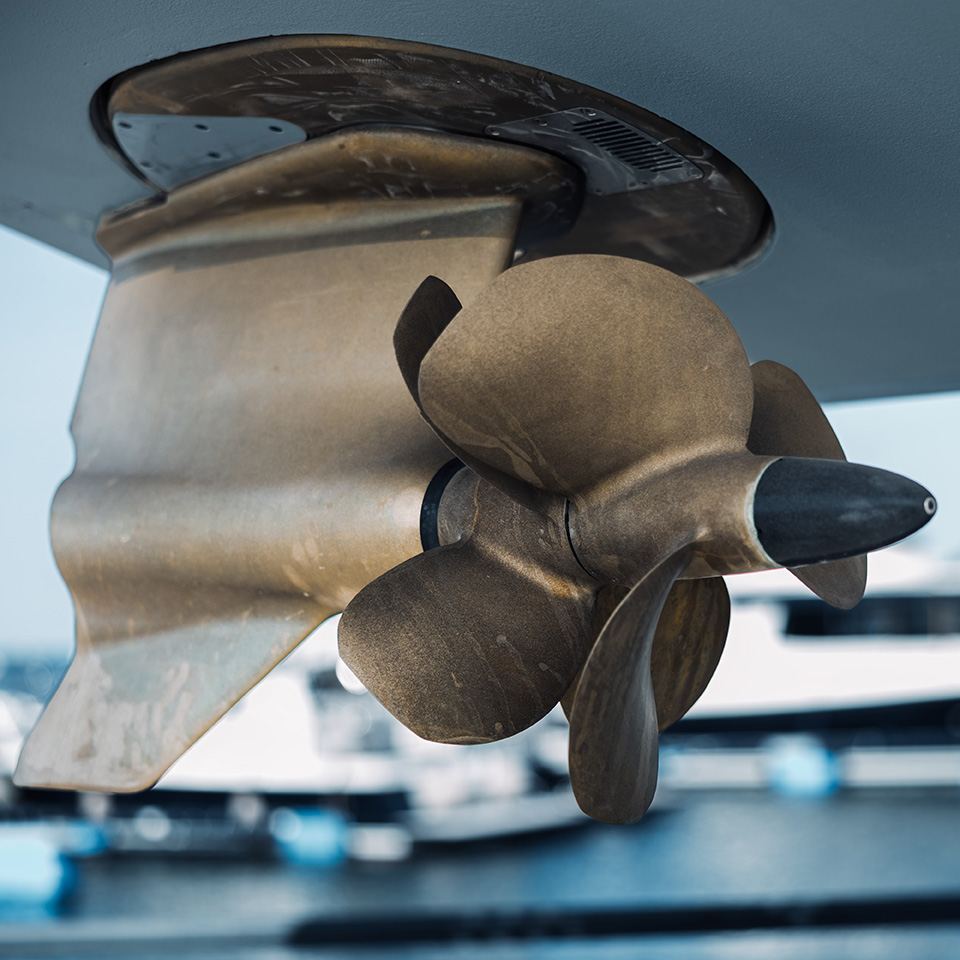 A Volvo Penta IPS pod drive with twin bronze propellers mounted under a boat hull, moored boats blurred behind
